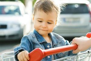 menino bonitinho sentado em um carrinho de compras foto