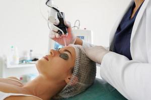 médico dermatologista e cliente mulher durante o tratamento de rejuvenescimento da pele a laser foto