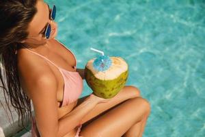 mulher relaxando na piscina e bebendo água de coco
