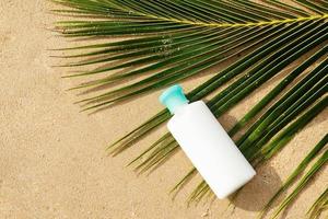 garrafa de loção de proteção solar e folha de palmeira na praia foto