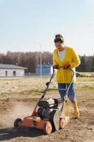 Aldeão de mulher está usando máquina de aerador para escarificação e aeração de gramado ou prado foto