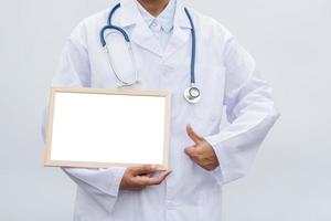 médico de profissão no jaleco branco sobre fundo branco isolado com placa branca em branco e polegares para cima. conceito de conceito de saúde, ciência e medicina foto