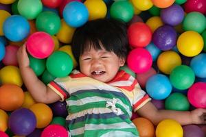 menina asiática feliz um ano e meio grande sorriso e jogando pequenas bolas coloridas na bola de bilhar. o conceito de brincar é o melhor aprendizado para as crianças. foto