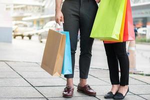 casal jovem feliz de compradores andando na rua comercial em direção e segurando sacolas coloridas na mão. conceito de venda e compras de sexta-feira negra foto