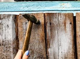 martelo em um cabo de madeira com ponta de metal. menina com manicure azul martelo pregos em uma cerca de madeira. mulher consertando a casa. mãos femininas estão envolvidas em assuntos masculinos foto