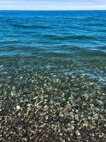 belas pedras redondas multicoloridas no mar, rios, lagos, lagoa, oceano e água fervente com ondas na praia rochosa de um resort quente tropical no horizonte e no céu. visão vertical foto