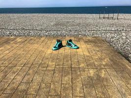 tênis esportivos verdes, sapatos em uma plataforma de madeira em uma praia arenosa contra o fundo do mar foto