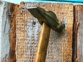 martelo em um cabo de madeira com ponta de metal. martelo pregos em uma superfície de madeira. pregos de metal são cravados em uma placa pintada de azul. construindo uma casa com martelo e pregos foto