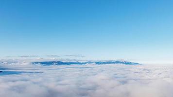 vale nas montanhas cobertas de neve acima do céu azul de nuvens. foto