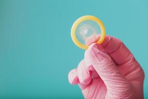 um preservativo aberto em uma mão em uma luva rosa segura em um fundo azul. látex para proteção contra a gravidez. foto