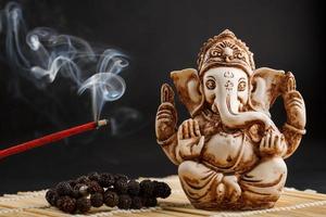 ganesha em um fundo preto. estátua e rosário com bastão de incenso fumegante vermelho foto