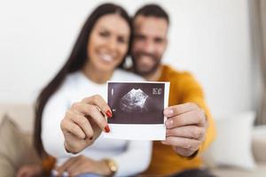 mulher e seu namorado segurando uma imagem de seu ultrassom do bebê. jovem casal feliz com ultrassom de bebê photo foto