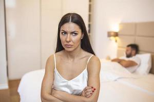 casal se ignorando na cama, jovem casal heterossexual infeliz no quarto. mulher triste sentada na beira da cama na frente do homem foto