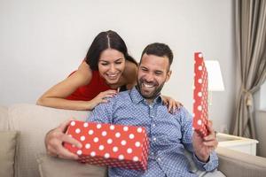 lindo casal jovem sorridente comemorando o amor no dia dos namorados ou aniversário. mulher atraente surpreendendo-o com um presente. foto