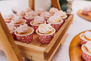 cupcakes gourmet com cobertura de creme de manteiga branco e confeitos em fundo de madeira foto