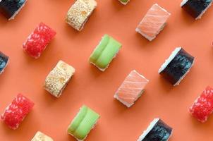 diferentes tipos de rolos de sushi asiáticos em fundo laranja. minimalismo vista superior plana padrão leigo com comida japonesa foto