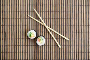 rolos de sushi e pauzinhos de madeira estão em uma esteira de serragem de palha de bambu. comida asiática tradicional. vista do topo. minimalismo plano leigo com espaço de cópia foto