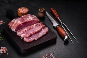 pedaço fresco de carne de porco crua com especiarias, sal e ervas em uma tábua de madeira