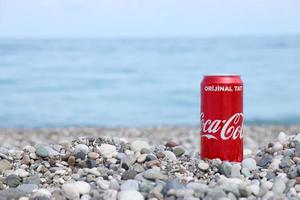 antalya, turquia - 18 de maio de 2022 lata vermelha original da coca cola encontra-se em pequenas pedras redondas perto da costa do mar. coca-cola na praia turca foto