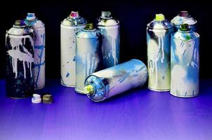 natureza morta com um grande número de latas de spray coloridas usadas de tinta aerossol na superfície de madeira tratada na oficina de grafite do artista. latas sujas e manchadas para arte em spray foto