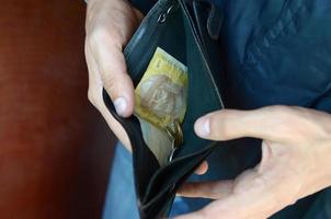 mãos masculinas com moedas com pequenas notas ucranianas e bolsa velha preta foto