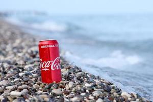 antalya, turquia - 18 de maio de 2022 lata vermelha original da coca cola encontra-se em pequenas pedras redondas perto da costa do mar. coca-cola na praia turca foto