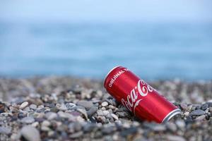 antalya, turquia - 18 de maio de 2022 lata vermelha original da coca cola encontra-se em pequenas pedras redondas perto da costa do mar. coca-cola na praia turca foto