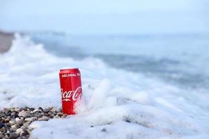 antalya, turquia - 18 de maio de 2022 lata vermelha original da coca cola encontra-se em pequenas pedras redondas perto da costa do mar. coca-cola na praia turca foto