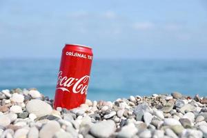 antalya, turquia - 18 de maio de 2022 lata vermelha original da coca cola encontra-se em pequenas pedras redondas perto da costa do mar. coca-cola na praia turca foto