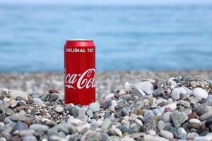 antalya, turquia - 18 de maio de 2022 lata vermelha original da coca cola encontra-se em pequenas pedras redondas perto da costa do mar. coca-cola na praia turca foto