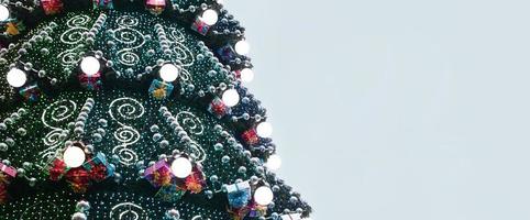 um fragmento de uma enorme árvore de natal com muitos enfeites, caixas de presente e lâmpadas luminosas. foto de um close de árvore de natal decorada com espaço de cópia