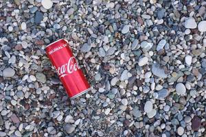 antalya, turquia - 18 de maio de 2022 lata vermelha original da coca cola encontra-se em pequenas pedras redondas perto da costa do mar. coca-cola na praia turca foto