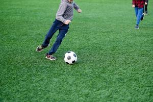 o menino joga futebol no quintal, no gramado. criança chuta a bola de perto foto