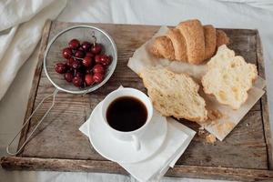 saboroso café da manhã com croissant fresco, café, cerejas em uma bandeja de madeira. croissant saudável com tomate e queijo. café expresso em uma bandeja de café da manhã foto
