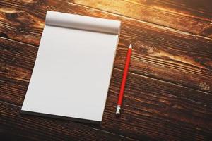 caderno com um lápis vermelho sobre um fundo marrom com sol quente, para escrever. espaço vazio livre para escrever em uma folha em branco de um caderno. foto