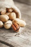 pecans derramam de um saco em uma mesa de madeira, close-up. descascado, em uma casca. foto