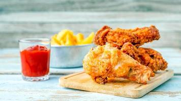 close-up de comida de frango frito e coxas de frango frito com batatas fritas e ketchup de tomate em uma mesa de madeira foto