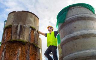 engenheiro controlando a qualidade da água fica nas escadas arriscadas em lugares altos operando equipamento industrial de purificação ou filtragem de água tanques de cimento antigos para manter a água na fábrica de água foto