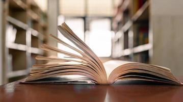 um livro aberto ou livro didático na biblioteca com luz da janela na mesa de leitura e o corredor das estantes no fundo da sala de aula da escola. conceito de aprendizagem educacional foto