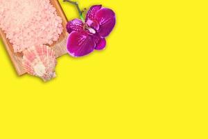 tigela de madeira com sal marinho rosa e orquídea roxa em fundo amarelo. beleza e spa. copie o espaço foto
