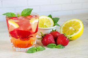 uma bebida refrescante de verão com gelo, morangos e limão em um fundo de madeira. o conceito de bebida de frutas. foto