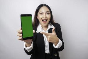 uma jovem empresária feliz está vestindo terno preto, mostrando espaço de cópia em seu telefone isolado por fundo branco foto