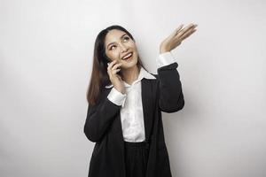 excitada empresária asiática vestindo terno preto apontando para o espaço da cópia em cima dela enquanto falava ao telefone, isolado pelo fundo branco foto