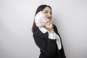 uma jovem empresária feliz está vestindo terno preto e segurando dinheiro em rúpia indonésia isolado por fundo branco foto