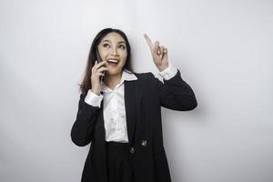 excitada empresária asiática vestindo terno preto apontando para o espaço da cópia em cima dela enquanto falava ao telefone, isolado pelo fundo branco foto