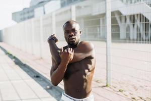 bonito homem afro-americano fazendo alongamento antes de um treino ao ar livre foto