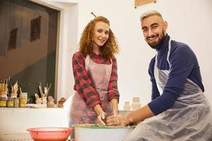 casal adorável sorrindo formando um vaso em um local de trabalho de cerâmica foto