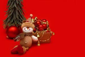 boneco de neve de brinquedo ao lado de brinquedos de natal e abeto em fundo vermelho com espaço de cópia, conteúdo de natal foto
