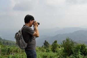 um homem asiático com sua mochila e câmera viaja sozinho e tira fotos na natureza montanhosa do lado do campo, conceito de viagem e meio ambiente, copie o espaço para texto individual