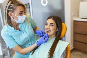 dentistas comparando a cor dos dentes do paciente com amostras para tratamento de clareamento. octor usando amostras de cores para mostrar bom resultado após o clareamento dos dentes foto